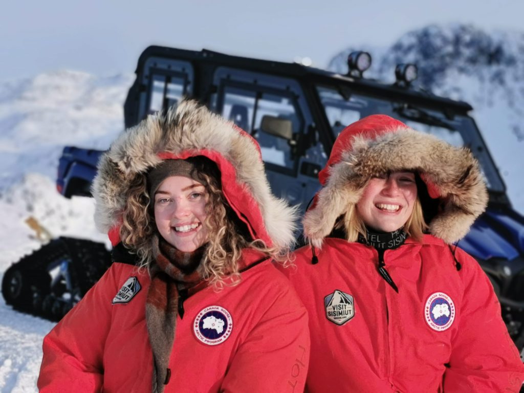 Two tourists on a winter UTV tour with the UTV iin the background