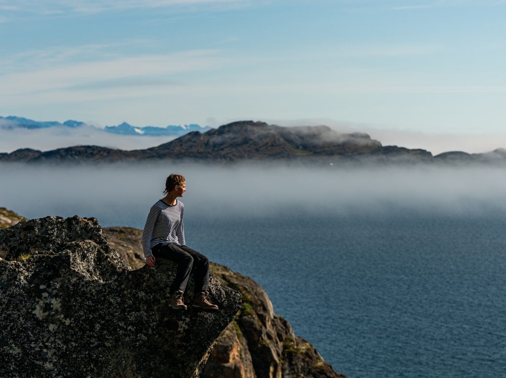 Hiker overlooking a fjord from the top of a mountain near Sisimiut